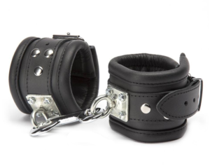A pair of Deluxe Leather Rotational Wrist Cuffs with metal buckles and D-rings. They are connected by a short silver chain with a clip. The interior lining of the restraints appears to be padded for comfort.