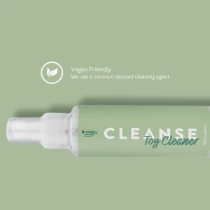 A bottle labeled "Loving Joy Cleanse Toy Cleaner" with a green label lies on a matching green background. Text reads, "Vegan Friendly. We use a coconut-derived cleaning agent," accompanied by a leaf icon above the text.