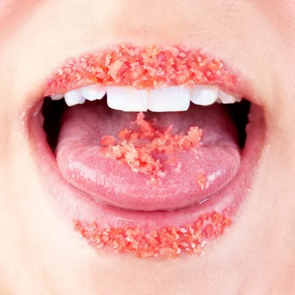 A close-up of a person's open mouth with coarse red Secret Play Explosive Kiss Oral Sex Popping Candies on their lips and tongue.