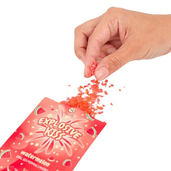 A hand sprinkles bright red Secret Play Explosive Kiss Watermelon Oral Sex Popping Candies from an opened packet against a white background.