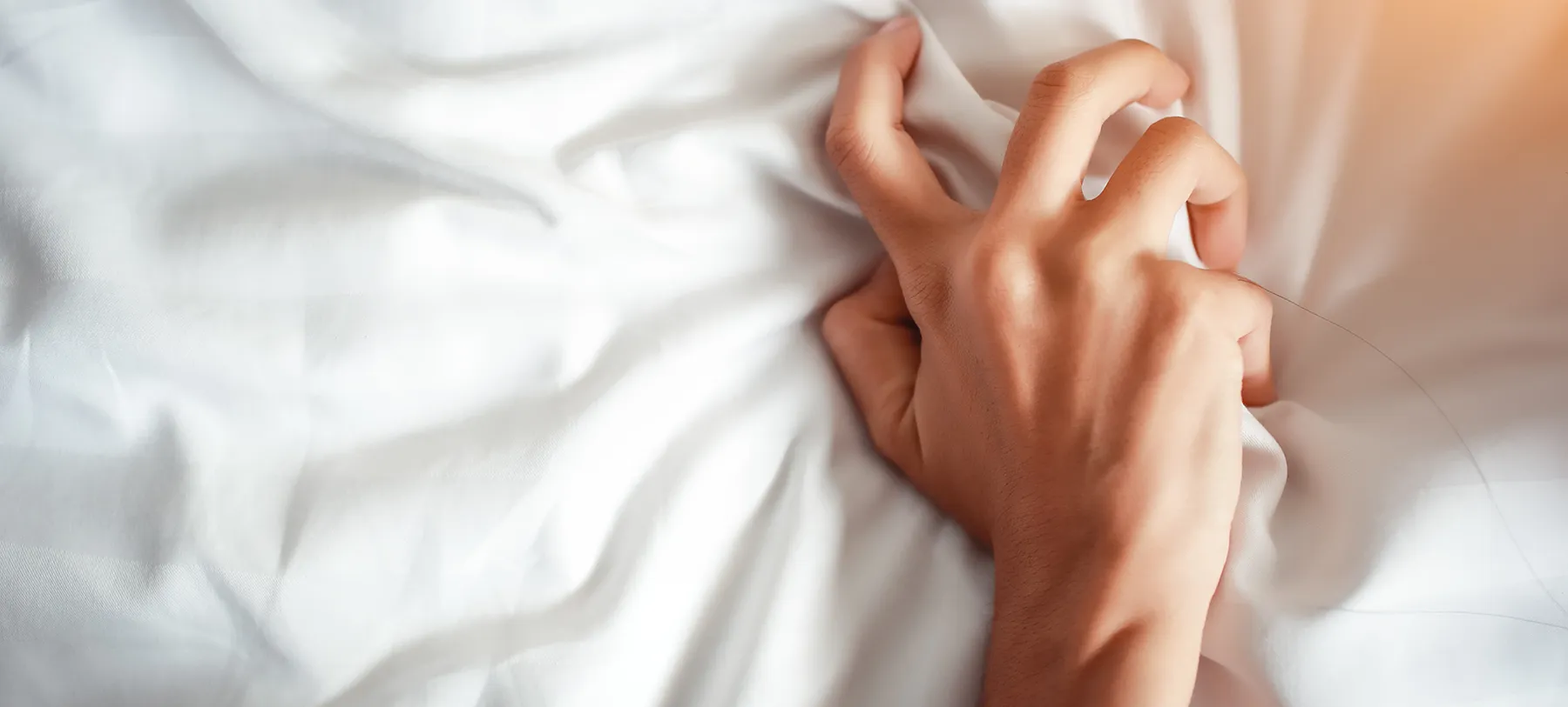 womans hand grabbing bed sheets in pleasure