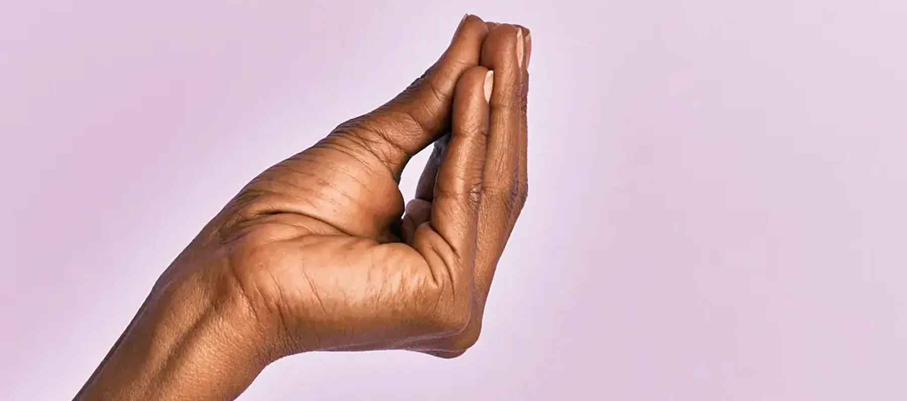 A hand with medium-dark skin tone is held up against a light purple background. The fingers are pressed together and slightly bent, resembling an Italian hand gesture often used to signify asking "what" or indicating something important.
