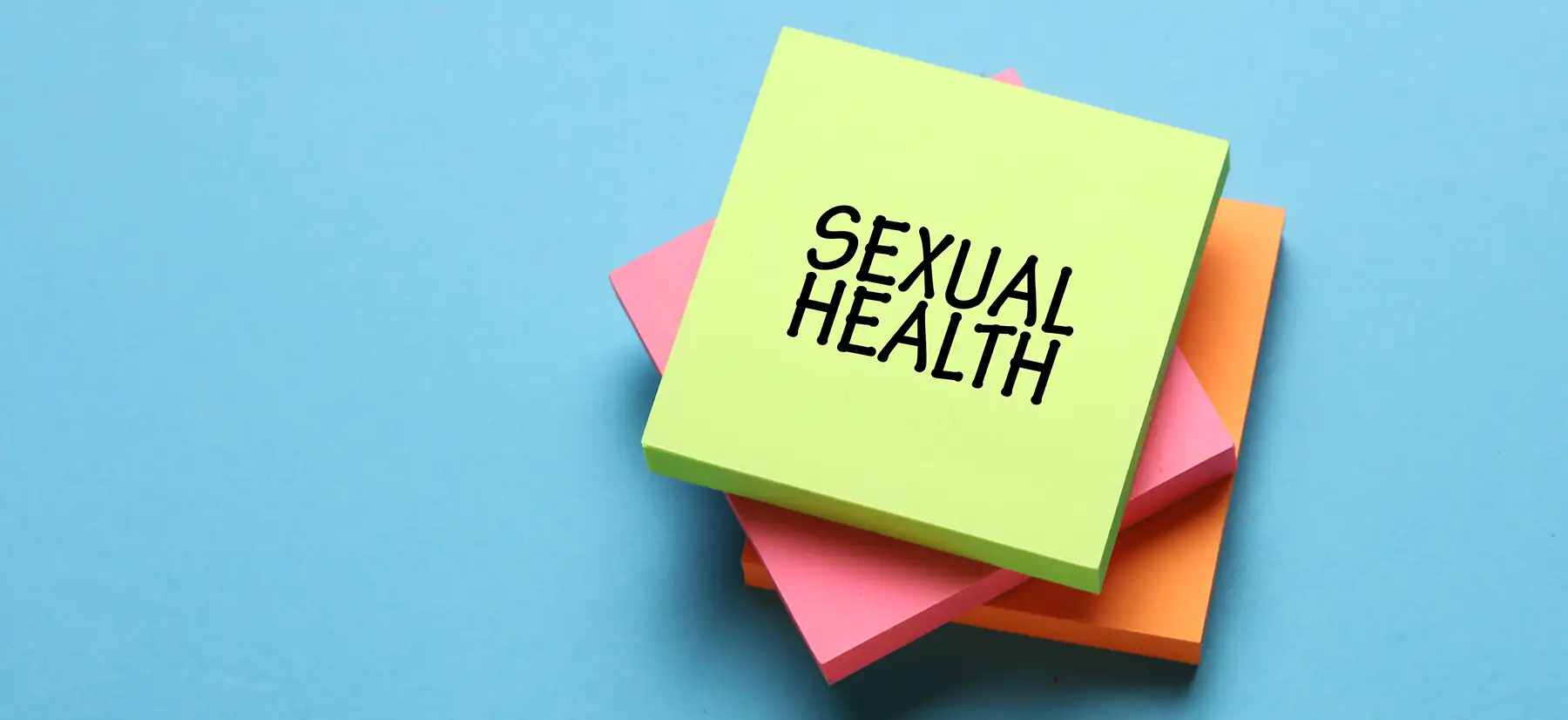 A stack of colourful sticky notes with the top note being light green and displaying the bold black text, "SEXUAL HEALTH," against a light blue background.