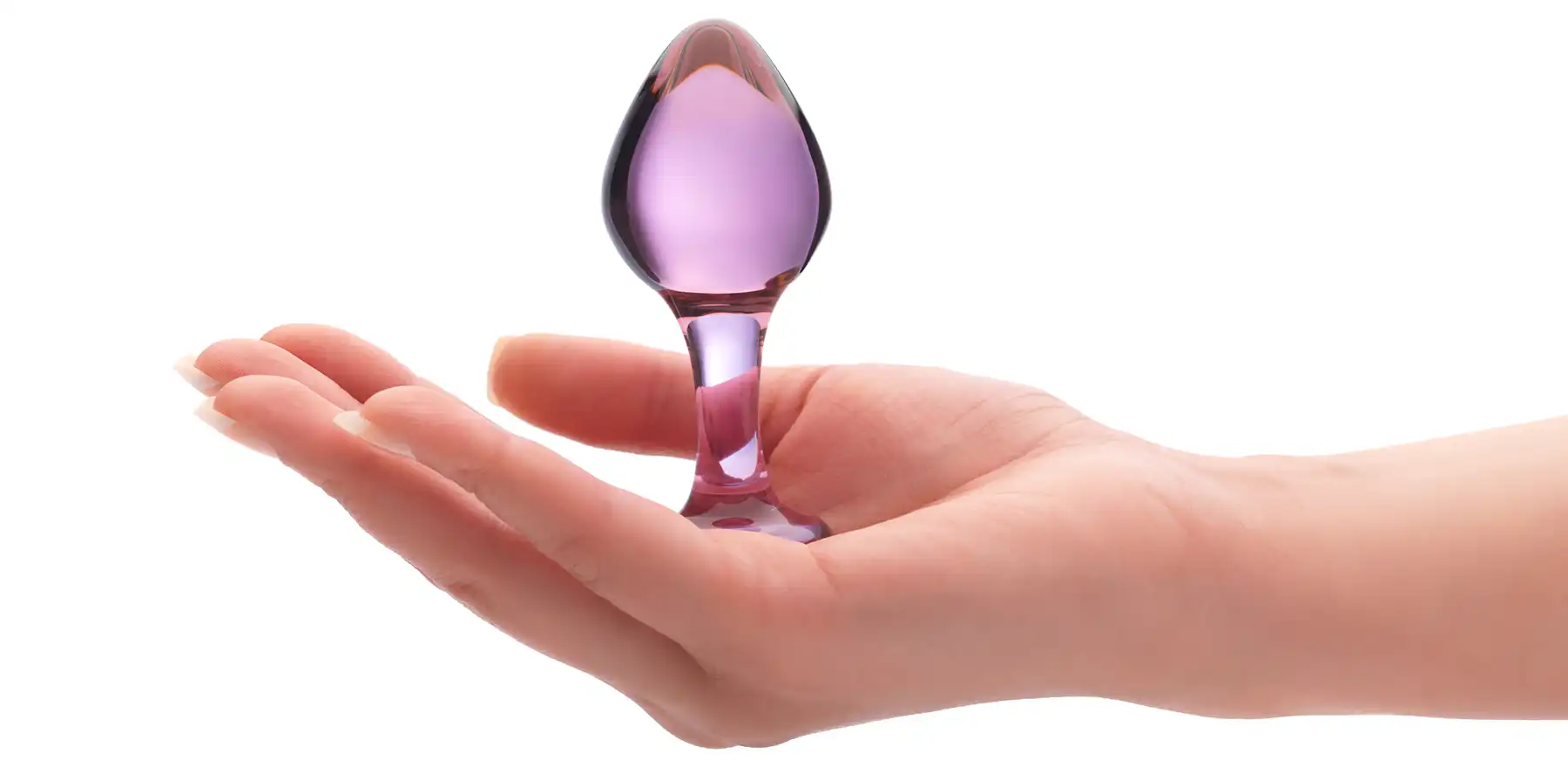 A hand is holding a small, translucent, purple glass butt plug shaped like a teardrop with a flared base. The anal sex toy is centred in the palm, with a white background.
