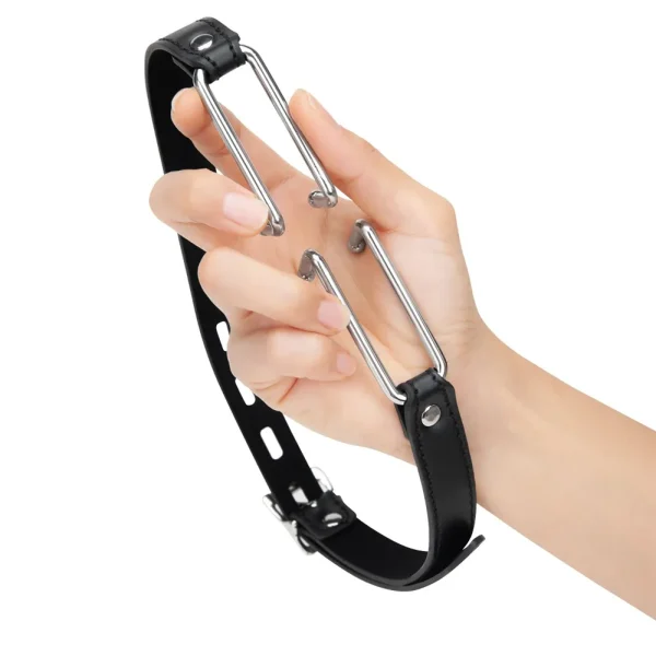 A hand holds the Me You Us Spider Gag 2, featuring a black PU leather strap with silver adjustable hooks. The gag includes a buckle and multiple holes for size adjustment.