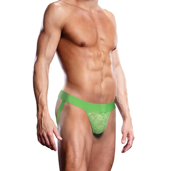 A shirtless model showcases the Prowler Lace Jock Strap in neon green, emphasising their muscular build. The underwear, adorned with a floral pattern and side straps linked to the waistband, stands out against a plain white background.