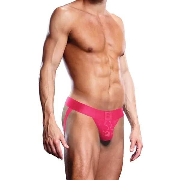 A muscular male model showcases the Prowler Lace Jock Strap in pink against a plain white background. The jockstrap, featuring wide straps and a contoured pouch, is in focus while the model's head is cropped out of the frame.