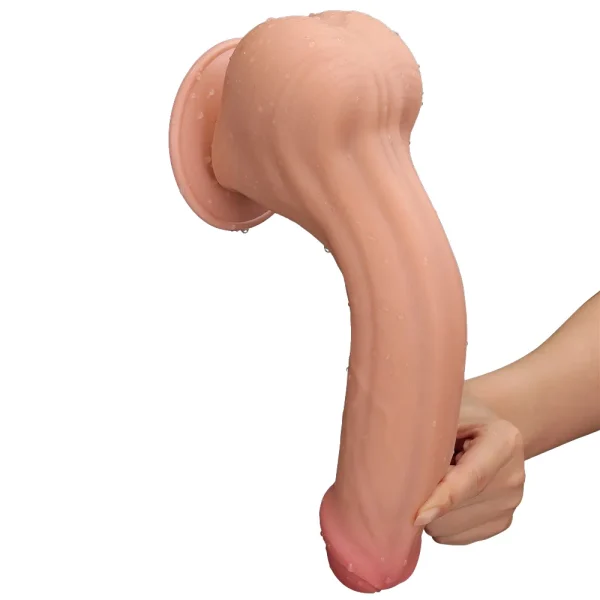 A hand holds the Sliding Skin King Sized 11.5 inch Dual Layer Dildo, showcasing its realistic, flesh-toned look, suction base, and flexible design against a plain white background. The toy appears slightly wet.