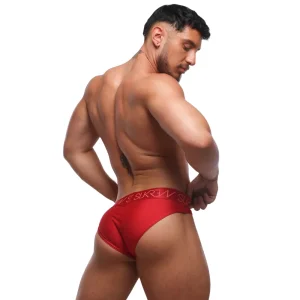 A muscular man poses with his back to the camera, wearing Sukrew Liberty Red Classic Briefs with a branded waistband, glancing over his shoulder against a plain white background.
