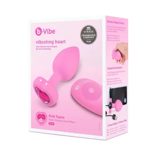 A box for the b-Vibe Vibrating Heart Remote Controlled Butt Plug, a pink, heart-shaped plug with jeweled base and remote. The packaging lists features and shows a hand holding the product.