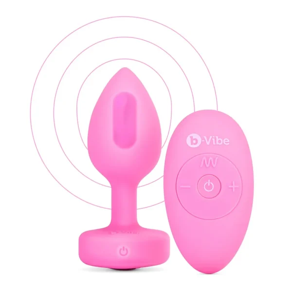 The b-Vibe Vibrating Heart Remote Controlled Butt Plug in pink comes with a matching pink wireless remote, both featuring simple controls and b-Vibe branding. Concentric lines in the background highlight their wireless connectivity.