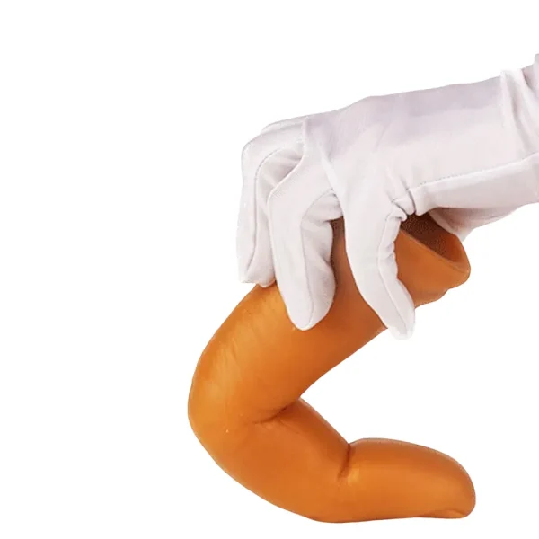 A gloved hand holds the Midas Touch Gold Finger Silicone Dildo, showing its flexibility, against a white background.