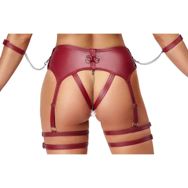 Close up of the bottom of a person wearing the Cottelli Bondage Wireless Bra & Crotchless Suspender Thong Set, a red leather harness with straps and chains around the waist, thighs, and arms, featuring an open back and a decorative jewel detail.