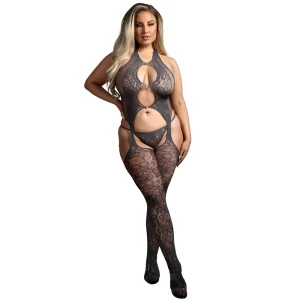 A woman models the Fantasy Lingerie Plus Size Worth The Wait Floral Fishnet Halter Bodystocking, featuring grey sheer lace and cutout details, with attached matching stockings, against a white background.