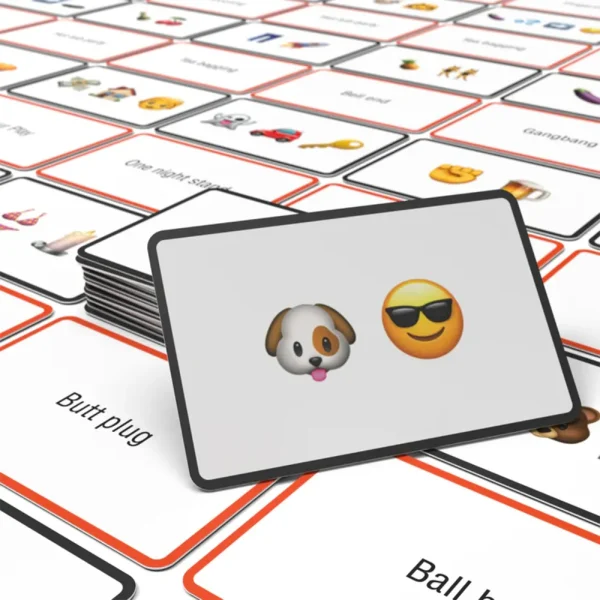 A stack of Name The Emoticon X Rated Card Game cards is on a table. The top card shows a dog face emoji and a sunglasses emoji, with more illustrated cards featuring words and emojis spread in the background.