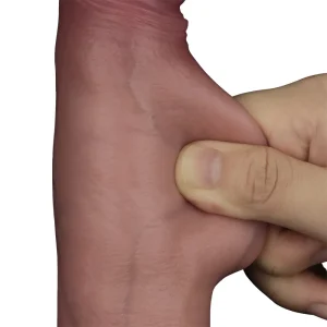 A hand pinches and pulls the skin on the Sliding Skin Pro II Realistic 8.5 Inch Dual Layer Silicone Dildo, demonstrating its stretchiness and elasticity (skin like design) against a plain white background.