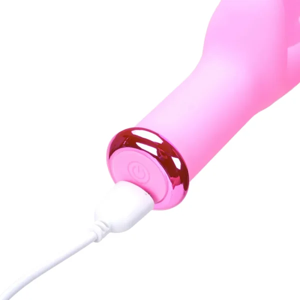 A close-up of the Maia Toys Myla Rechargeable 10 Function Butterfly G-Spot Vibrator in pink, featuring a shiny metallic accent and a power button, being charged via a white cable connected to its base.