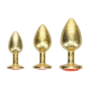The Ouch Milan Collection Anal Plug Set features three gold-colored, metallic, tapered plugs in graduated sizes. Each has a circular base with a red jewel base underneath and is shown upright against a white background.
