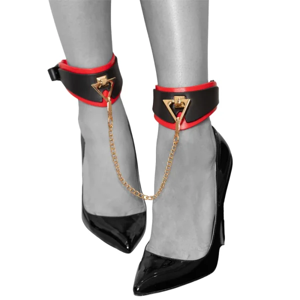 A person wearing black high heels and Ouch Milan Collection Leg Cuffs, black and red ankle cuffs linked by a gold coloured chain. The photo highlights their lower legs and feet against a simple backdrop.