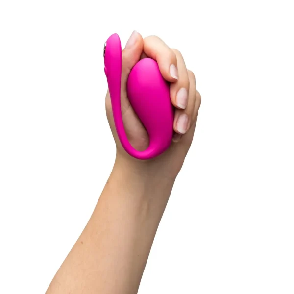 A hand holds the We-Vibe Jive 2 App Controlled Rechargeable Love Egg Vibrator, a bright pink, curved silicone g-spot vibrator, with a bulbous end and flexible tail, against a white background.