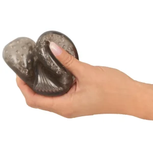 A hand squeezes a dark, textured masturbator from the Rebel 7-Piece Performance Sex Toy Set.