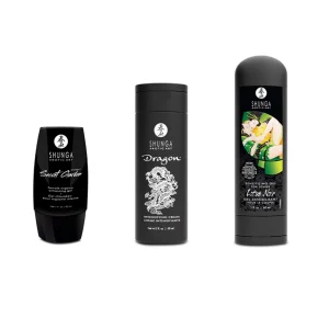 Three black bottles from the Shunga Calendar of Desires are displayed in a row, each with unique white designs and text. The third bottle features an illustrated couple in a green and yellow embrace.