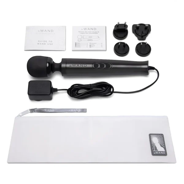 The Le Wand Diecast Plug In Vibrating Wand Massager contents, with a charger, three international plug adaptors, two instruction booklets, and a white zipped storage pouch featuring the logo, is displayed on a white background.