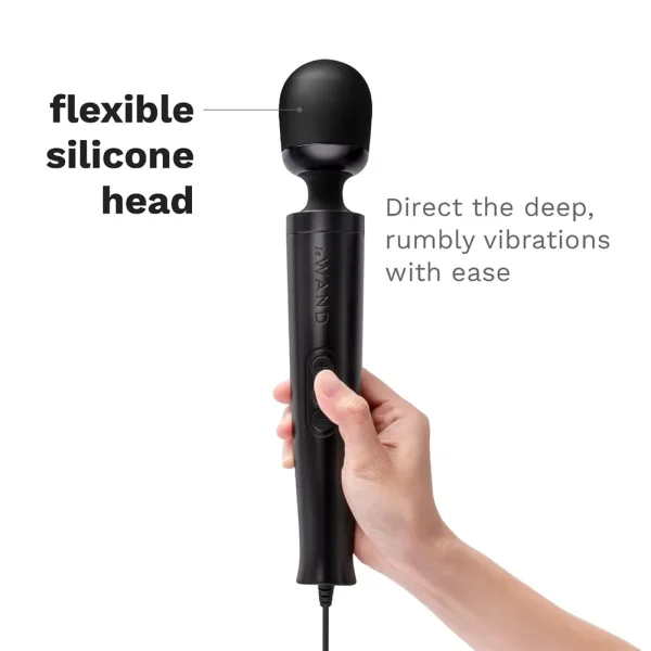 A hand holds the Le Wand Diecast Plug-In Vibrating Wand Massager with its flexible silicone head. Text highlights “flexible silicone head” and points to the wand, stating, “Direct deep, rumbly vibrations with ease.”.