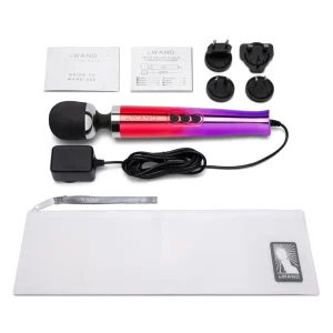The Le Wand Diecast Plug In Vibrating Wand Massager, shown in red to purple gradient with a black head, comes with power adaptors, instruction manuals, and a white storage pouch, all arranged on a white background.