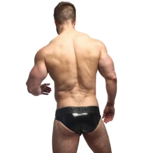 A muscular man stands with his back to the camera, modelling the Sukrew Fetish Black Wet Look Classic Brief, arms slightly bent, against a plain white background.