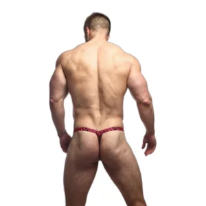 A muscular man standing with his back to the camera, wearing a red and black patterned thong, against a plain white background.