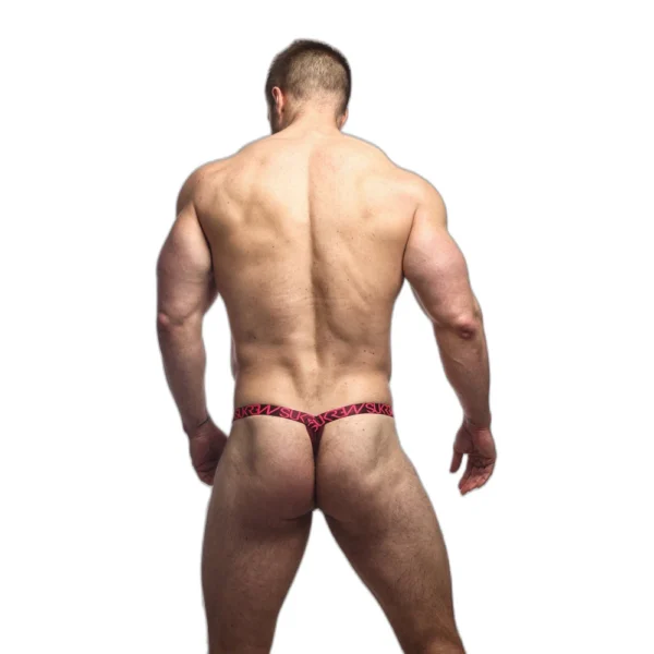 A muscular man standing with his back to the camera, wearing a red and black patterned thong, against a plain white background.