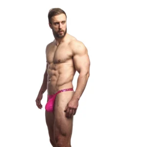 A muscular man with a beard poses against a white background, wearing only bright pink pants.