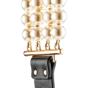 Close-up of a watch strap featuring three rows of large, glossy white pearls connected by a gold bar, attached to a textured black leather band with silver studs.