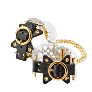 A pair of bracelets featuring rows of white pearls, black leather straps with gold buckles and eyelets, and a gold chain connecting the two pieces.