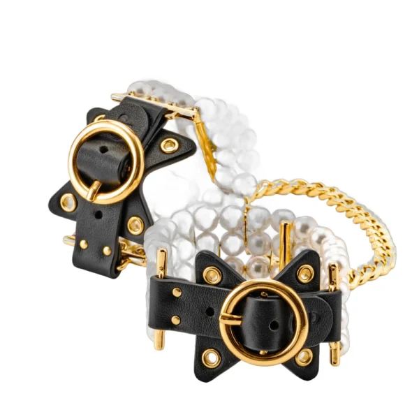A pair of bracelets featuring rows of white pearls, black leather straps with gold buckles and eyelets, and a gold chain connecting the two pieces.