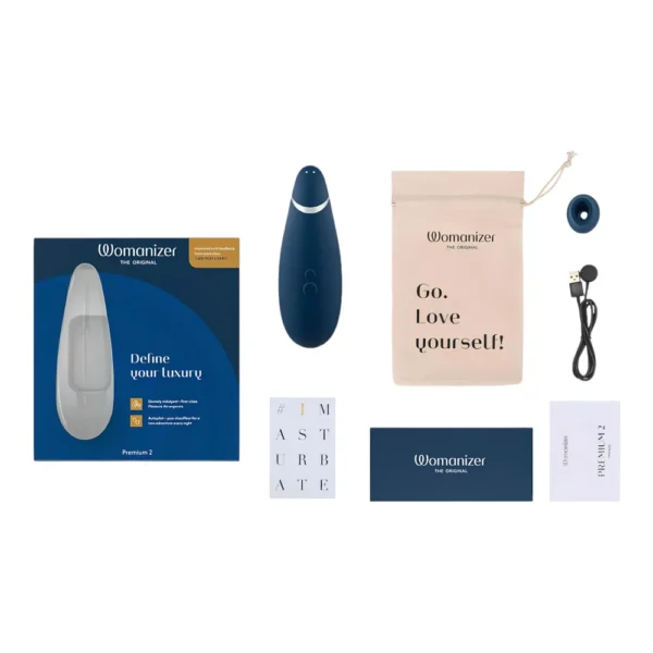 A blue Womanizer Premium 2 device with accessories, including a storage pouch, charging cable, extra head, instruction booklets, and product box, all neatly arranged on a white background.