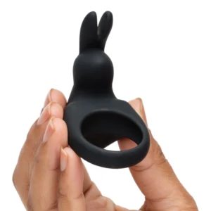 A hand holding a black silicone ring with a rabbit-shaped top, designed as an adult toy, against a plain background.