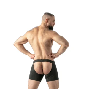 A muscular man poses with his back turned, wearing black shorts that have an open back, exposing his buttocks. The background is white.