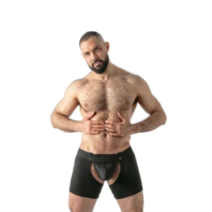 A muscular man with a beard poses bare-chested, wearing black boxer shorts with a large front cut-out, standing against a plain white background.