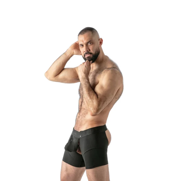 A bearded man poses confidently in black boxer shorts with a cut-out back, standing against a white background.