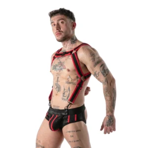 A tattooed man wearing a black and red harness, arm bands, and matching fetish gear poses against a plain white background.