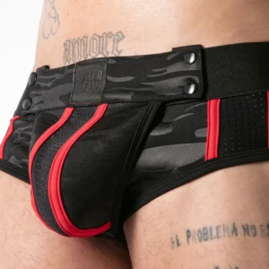 Close-up of a person wearing black and red camo-patterned underwear with mesh panels. Several tattoos are visible on their lower torso.